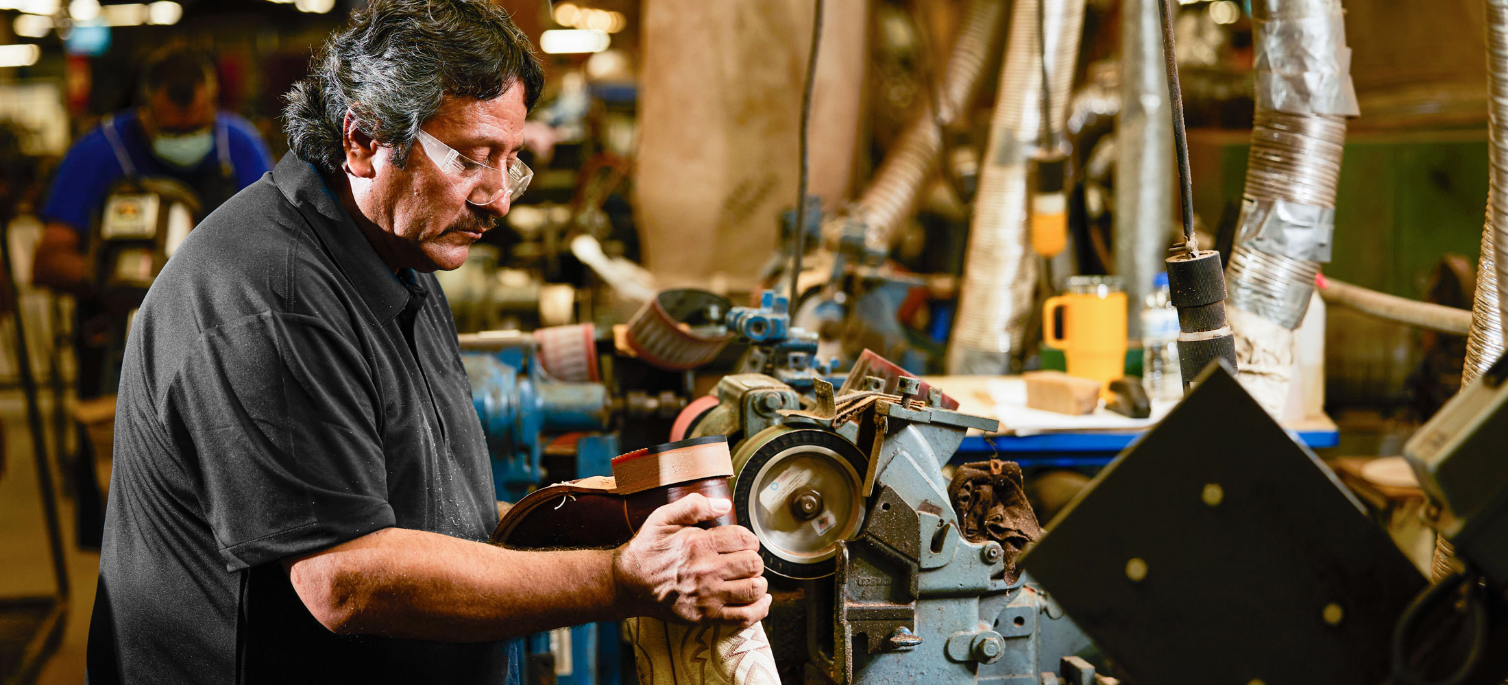 A man holding a boot turned facing a workbench.